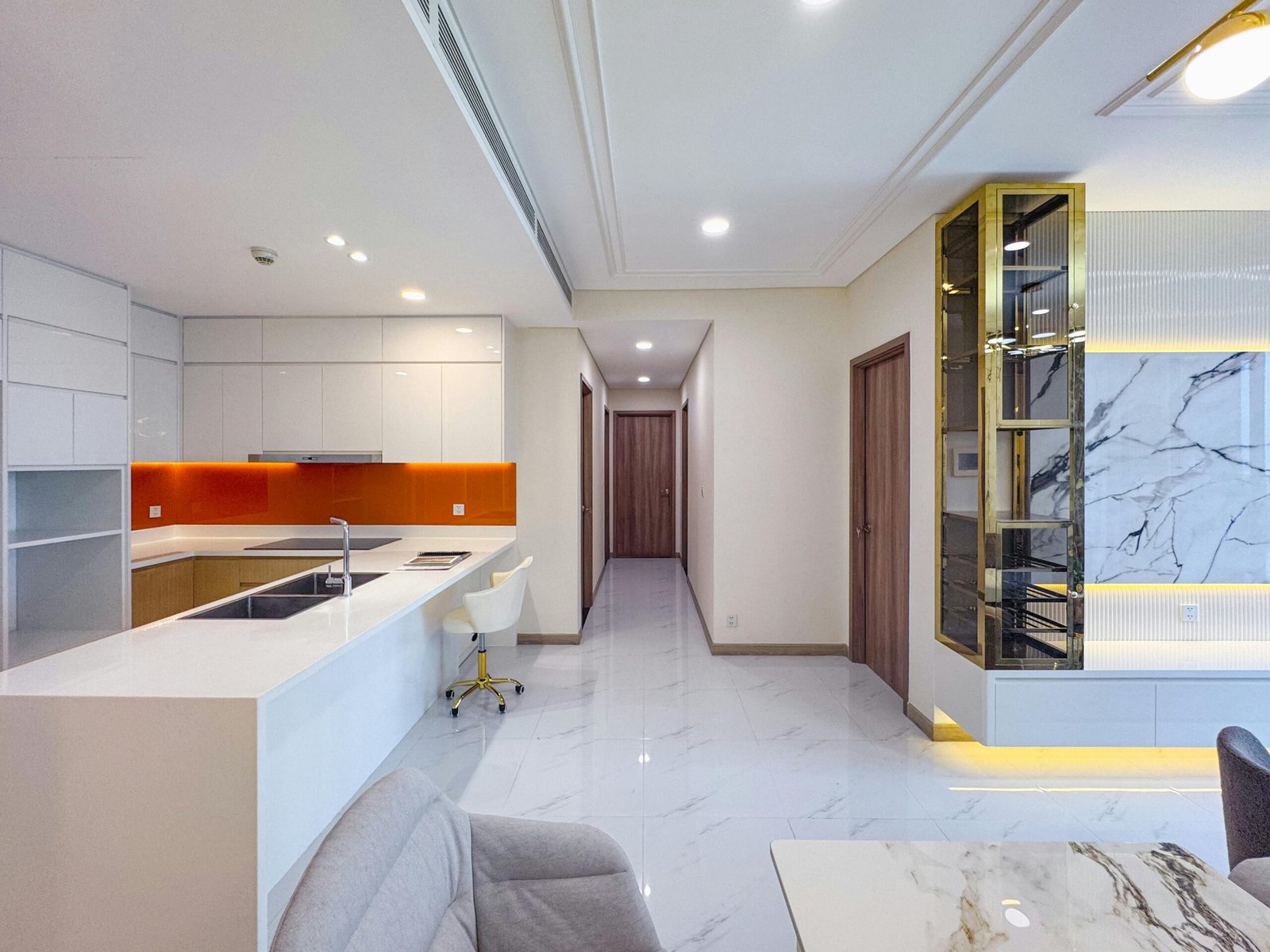 Contemporary open-plan kitchen and living space with marble decor and orange accents.